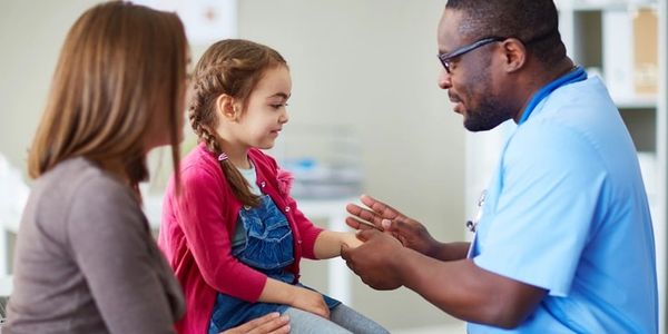 Pediatrician examines a smiling little girl with her mother present. Trusting pediatric care.