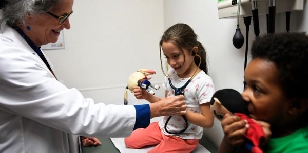 Pediatrician lets a little girl try on their stethoscope, sparking joy and trust.