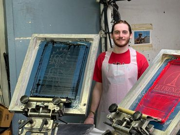 image of screenprinter standing at a printing press smiling