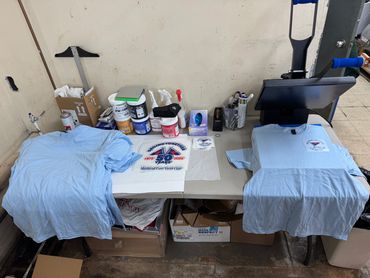 a table set up with a DTF heat clamp , t shirts and cut and organized DTFs ready to press