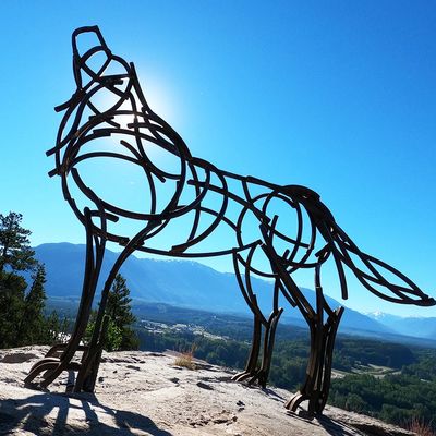 Metal wood sculpture of a wolf with a blue sky in the background.