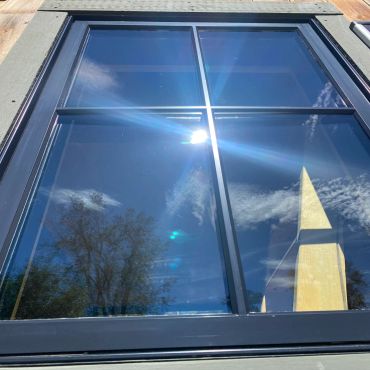 Window reflecting a tree and sky with sun glare.