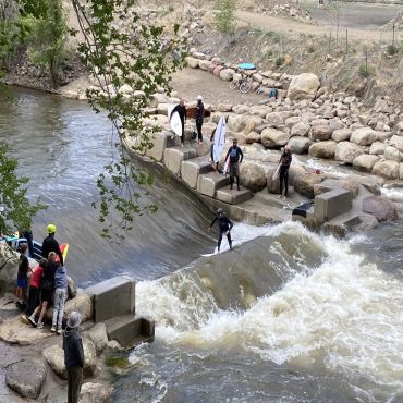 People surfing in a river wave surrounded by rocks.