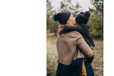 Mother kissing child while holding him outdoors in winter clothing.