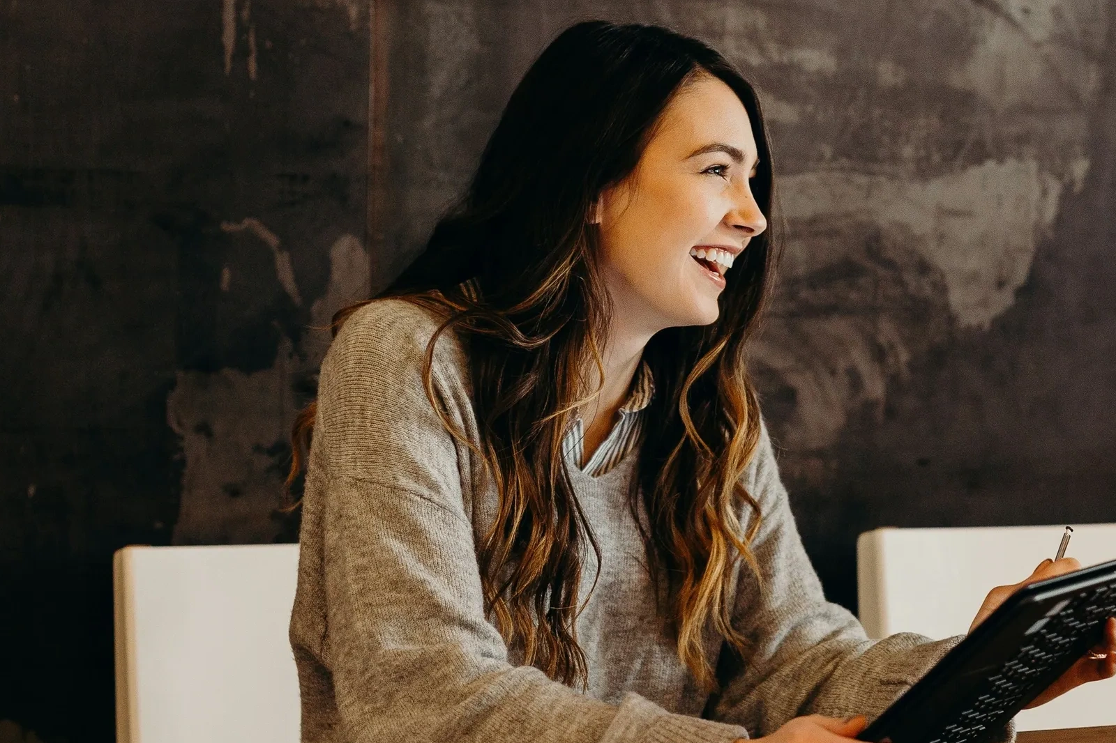 Young woman laughing and holding a tablet with a stylus.