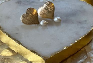Gold heart-shaped earrings with pearl drops on a white and gold stone surface.