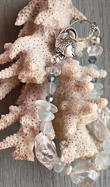 Silver fish charm bracelet with translucent beads on coral.