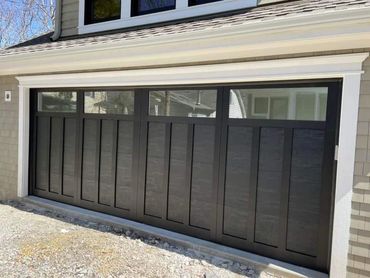 Modern black garage door with upper windows on a beige house.