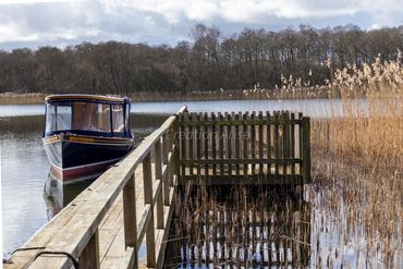 rollesby broad. Gentlemen Jim electric boat, landing decking, reeds, reflective broad.