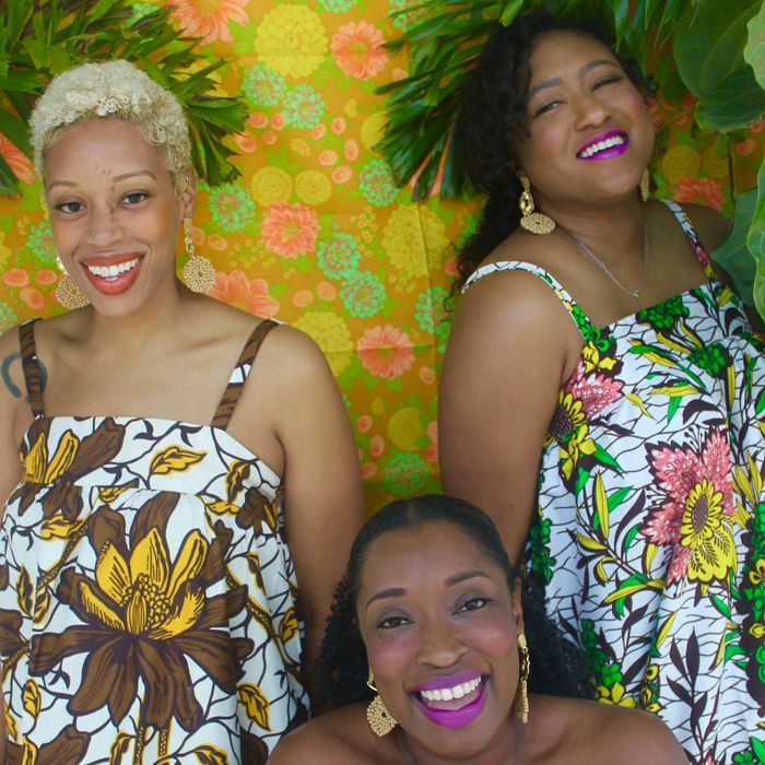 Three beautiful brown-skinned women in floral dresses laughing out loud.