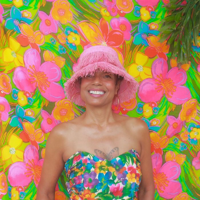 A brown-skinned woman smiling and wearing a floral bustier top with a neon floral background.
