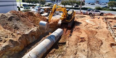 Excavator installing large concrete pipes at construction site.