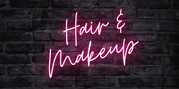 Neon sign that says "Hair & Makeup" on a brick wall.