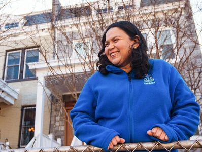 Woman with blue jacket smiling standing at fence outside house