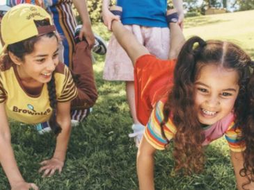 Kids playing a wheelbarrow race outdoors.