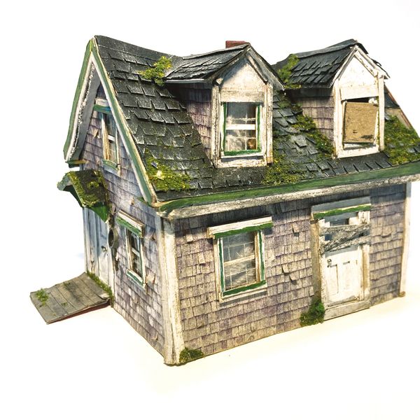 A small, detailed model of an old, weathered house with moss on the roof.