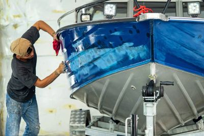 A man polishing the side of a blue boat indoors.