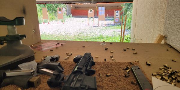 View from a shooting range booth with targets and firearms on the table.