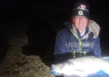 Person holding a large fish at night on a rocky shore.