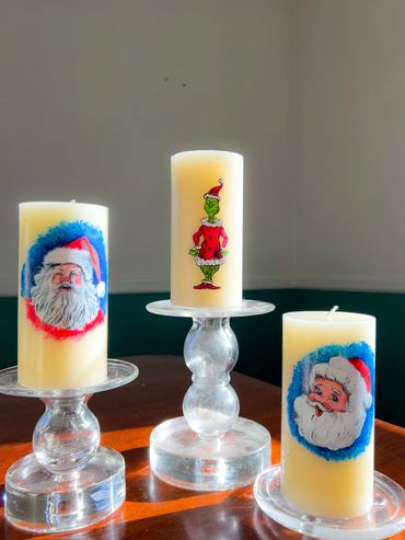 Three Christmas-themed candles with Santa and Grinch designs on glass holders.