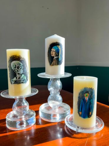 Three candles with famous art reproductions on glass holders.