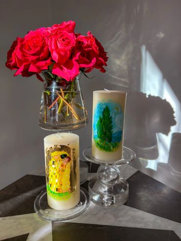 Vibrant red roses in a glass vase with two decorative candles on a marble surface.