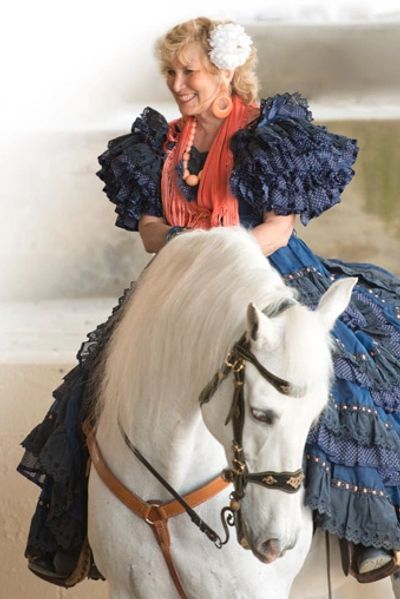 Woman in traditional dress riding a white horse.