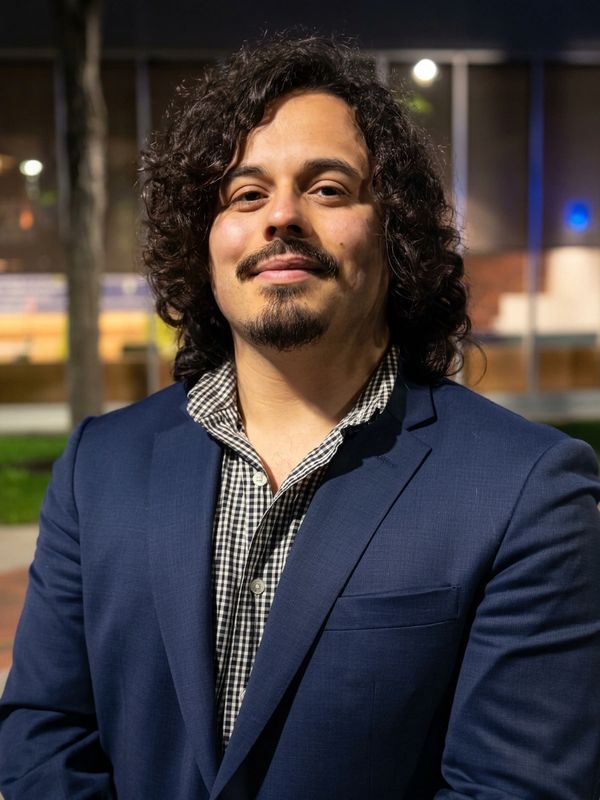 Man with curly hair wearing a blue suit jacket and checkered shirt.