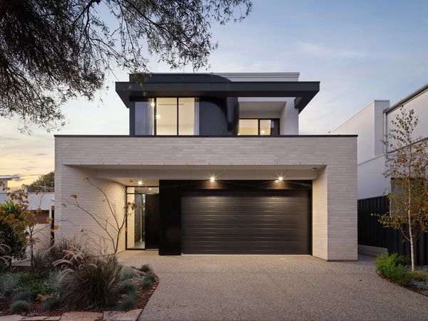 Modern two-story house with black garage door and beige brick exterior.