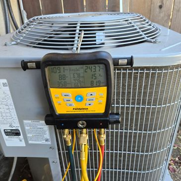 Fieldpiece refrigerant manifold gauge attached to an air conditioning unit.