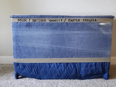 A wrapped antique vanity marked "MBR / ANTIQUE VANITY / SUPER FRAGILE,"