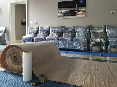 A living room with wrapped furniture, a roll of protective material, and tools