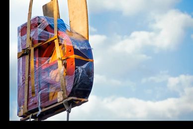 Wrapped piano being lifted against a blue sky with clouds.