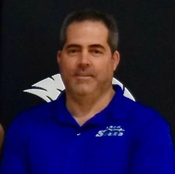 Man in blue polo shirt standing with hands clasped in front.