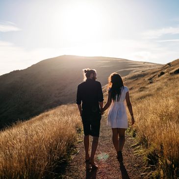 Couple walking hand in hand on a sunlit hillside path.