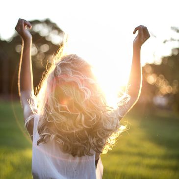 A person enjoys the sunlight with arms raised in a grassy field.