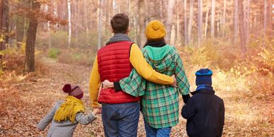 A family of one man, one woman and 2 children walking in the woods in fall.