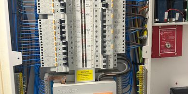 Open electrical fuse box with labeled switches and warning signs.