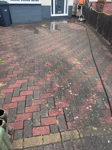 Person pressure washing a driveway with weeds and dirt.