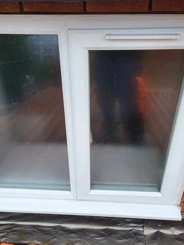 Frosted basement window with white frame set in a brick wall.