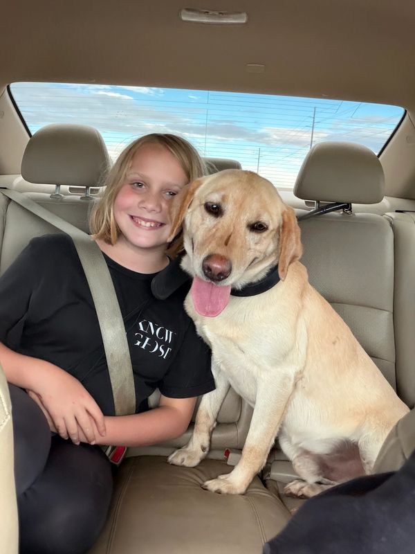 Child and dog sitting in car backseat smiling.
