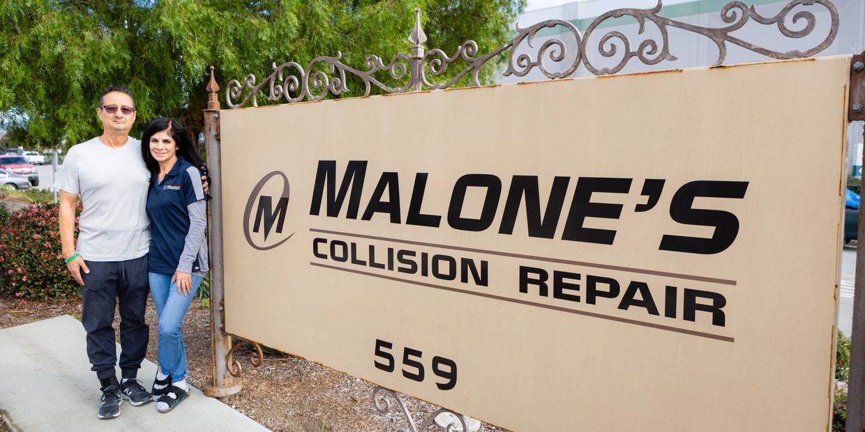 A couple standing next to a Malone's Collision Repair sign outside.