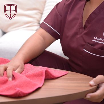 Person cleaning a wooden table with a red cloth, wearing a maroon uniform.