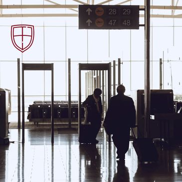Two travelers with luggage walking through airport security gates.