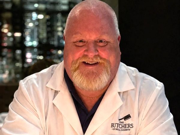 Smiling butcher wearing a white coat with logo.