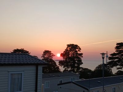 Sunset over houses and trees near the coast.