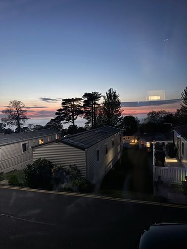 Sunset over mobile homes near trees and water.