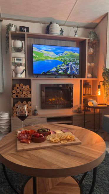Cozy living room with a TV, electric fireplace, and snacks on a wooden table.
