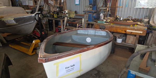 Small boat with 'For Sale' sign in workshop.
