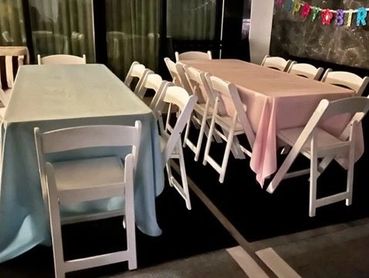 Two rectangular 6ft tables with pastel pink and light baby blue linens. White padded resin chairs set for a birthday party celebration. All the party supplies you need to create an affordable party needs for that special event planning.